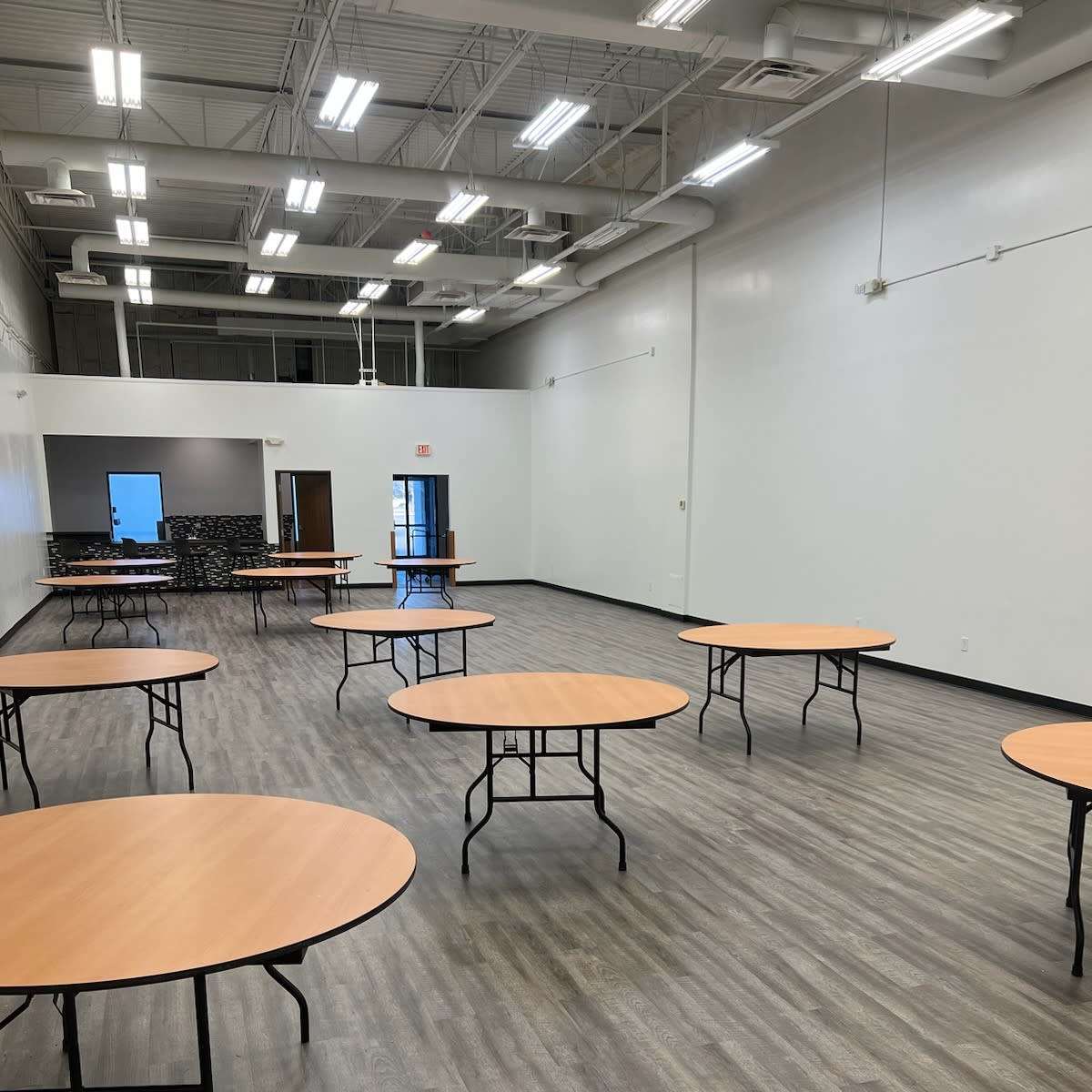 A spacious room with several round tables arranged on a wooden floor.