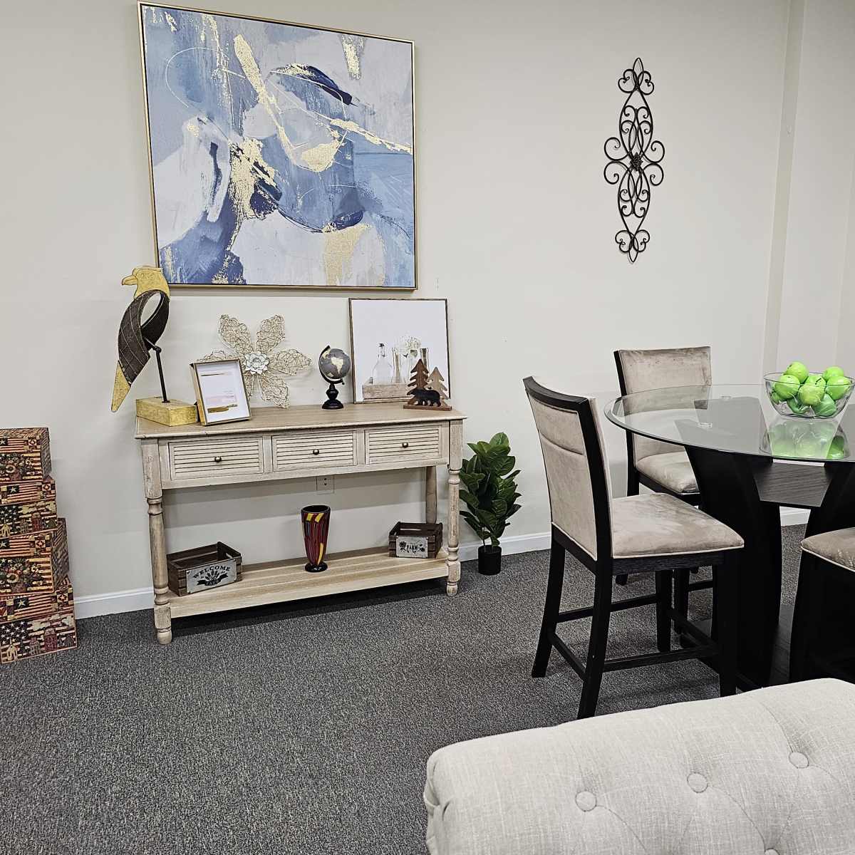 A neatly arranged modern dining area featuring a circular glass table surrounded by high-backed chairs, a side console table displaying decorative items, and artwork on the walls.