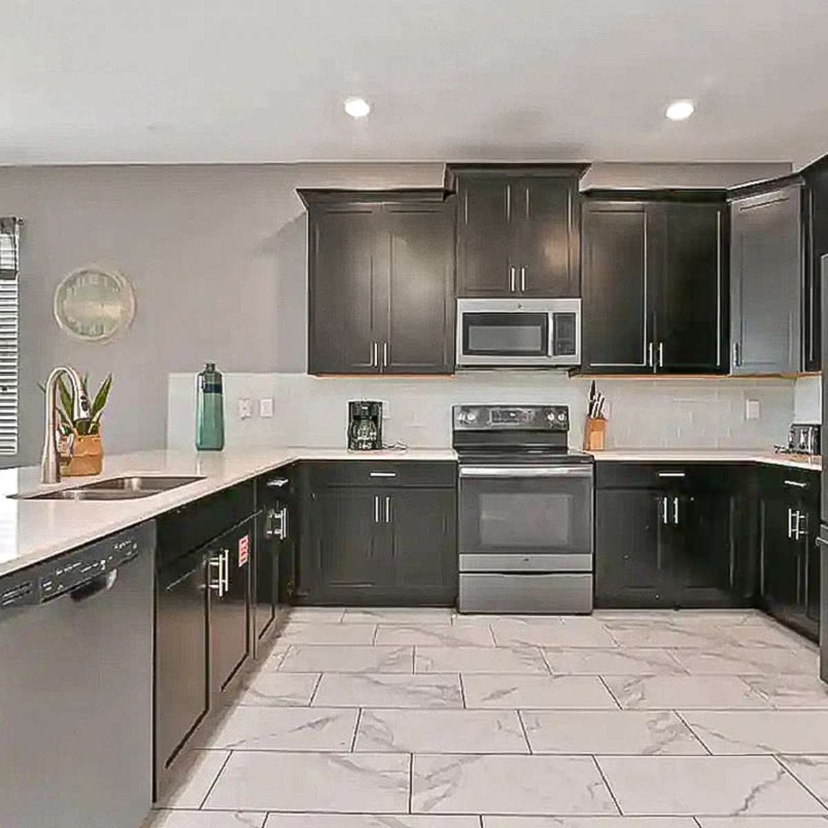 A modern kitchen with dark cabinetry, stainless steel appliances, and a light-colored countertop.