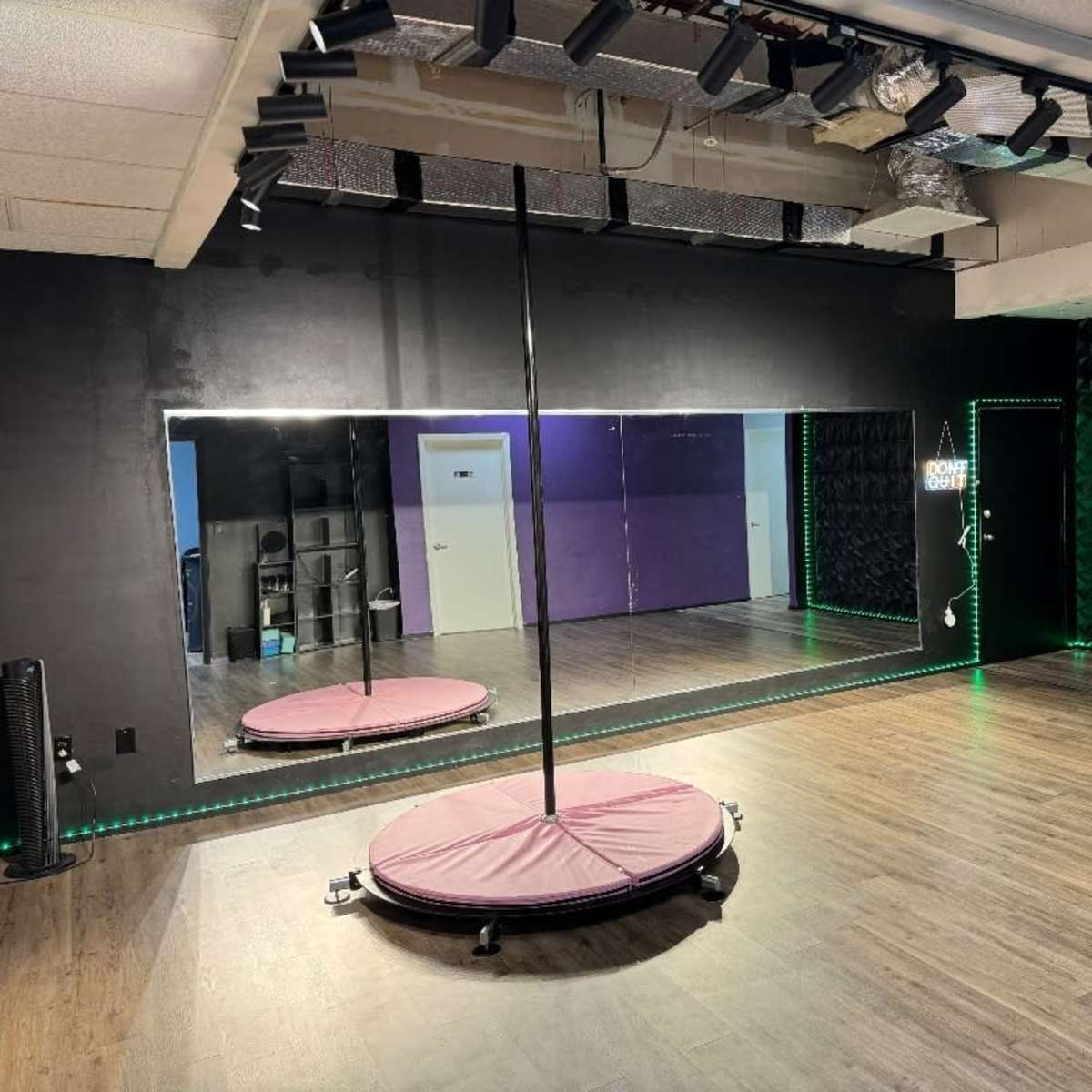 A dance studio featuring a mirrored wall, a central pole, and LED lighting along the edges of the room.