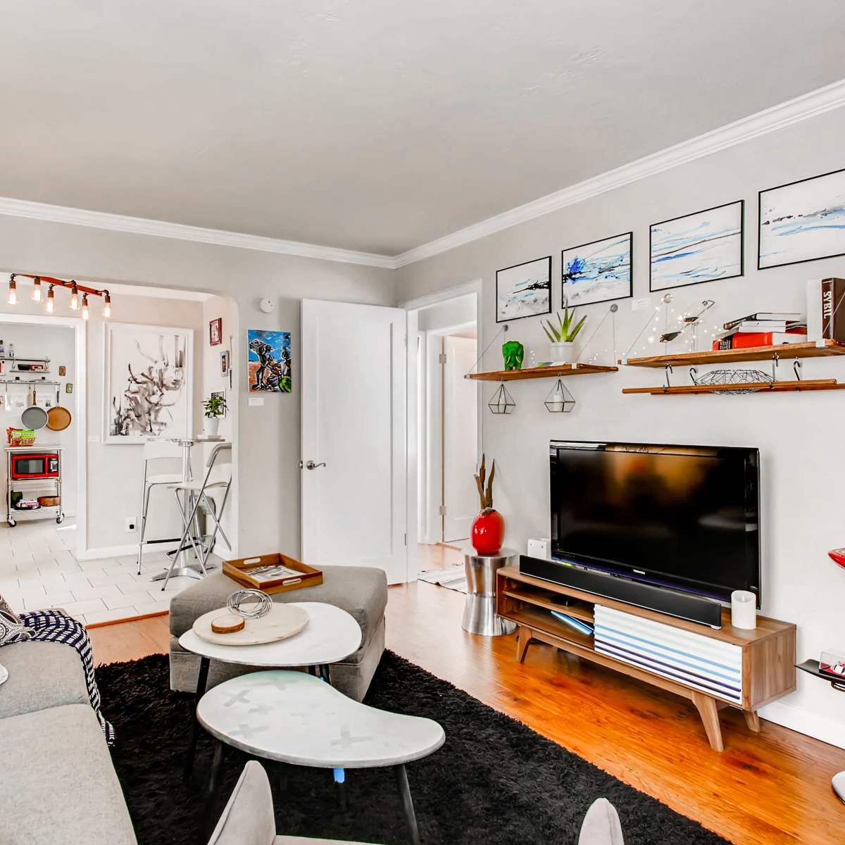 A modern living room with a gray sofa, a wall-mounted television on a wooden console, and decorative shelves displaying plants and artwork.