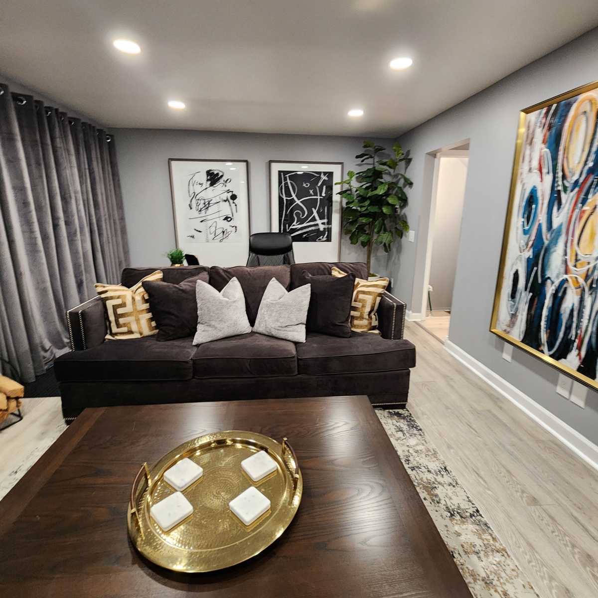 A modern living room featuring a dark sofa with decorative pillows, a wooden coffee table with a tray, and abstract wall art.