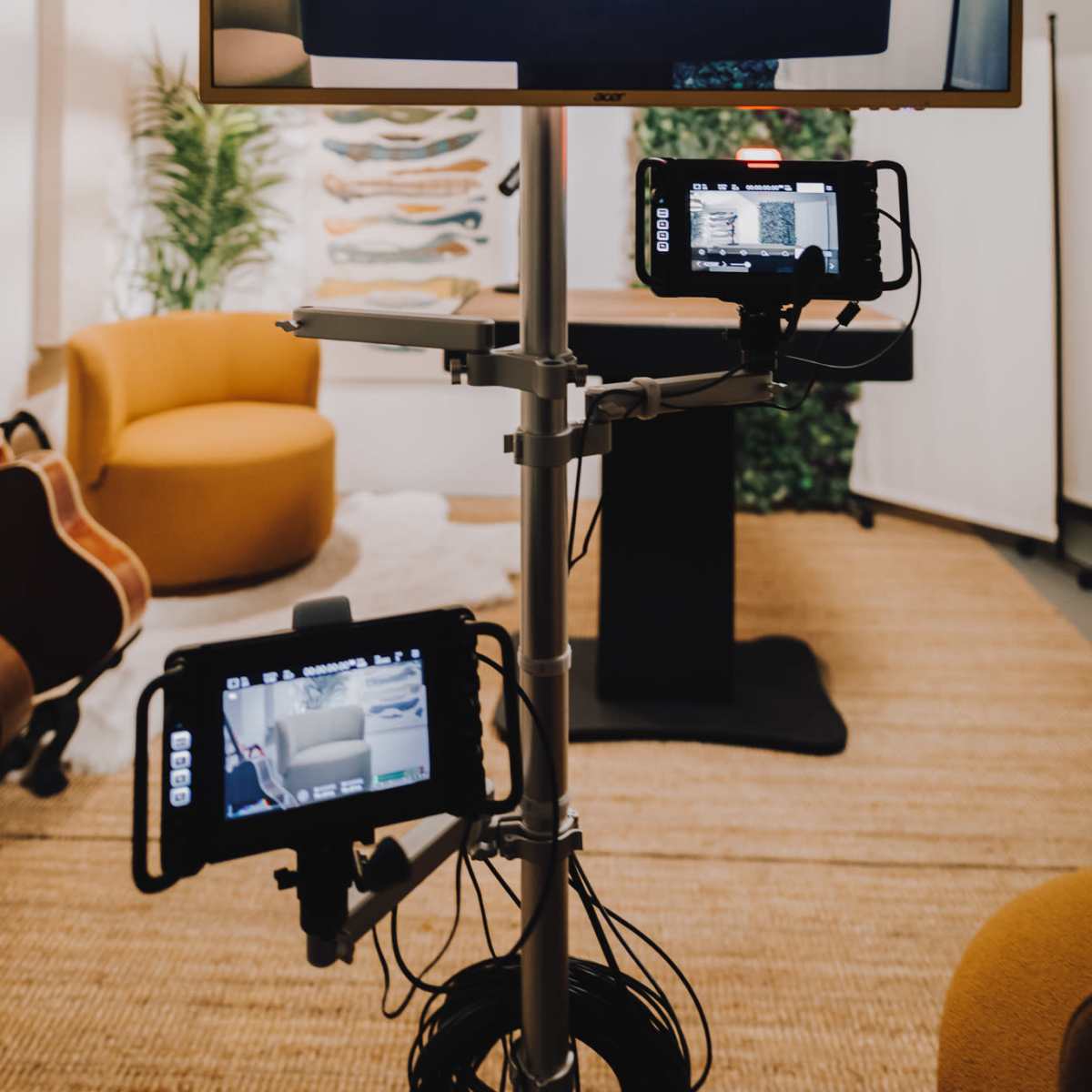 A mounted screen displays a table with microphones in a studio setting, featuring plants and cozy seating in the background.