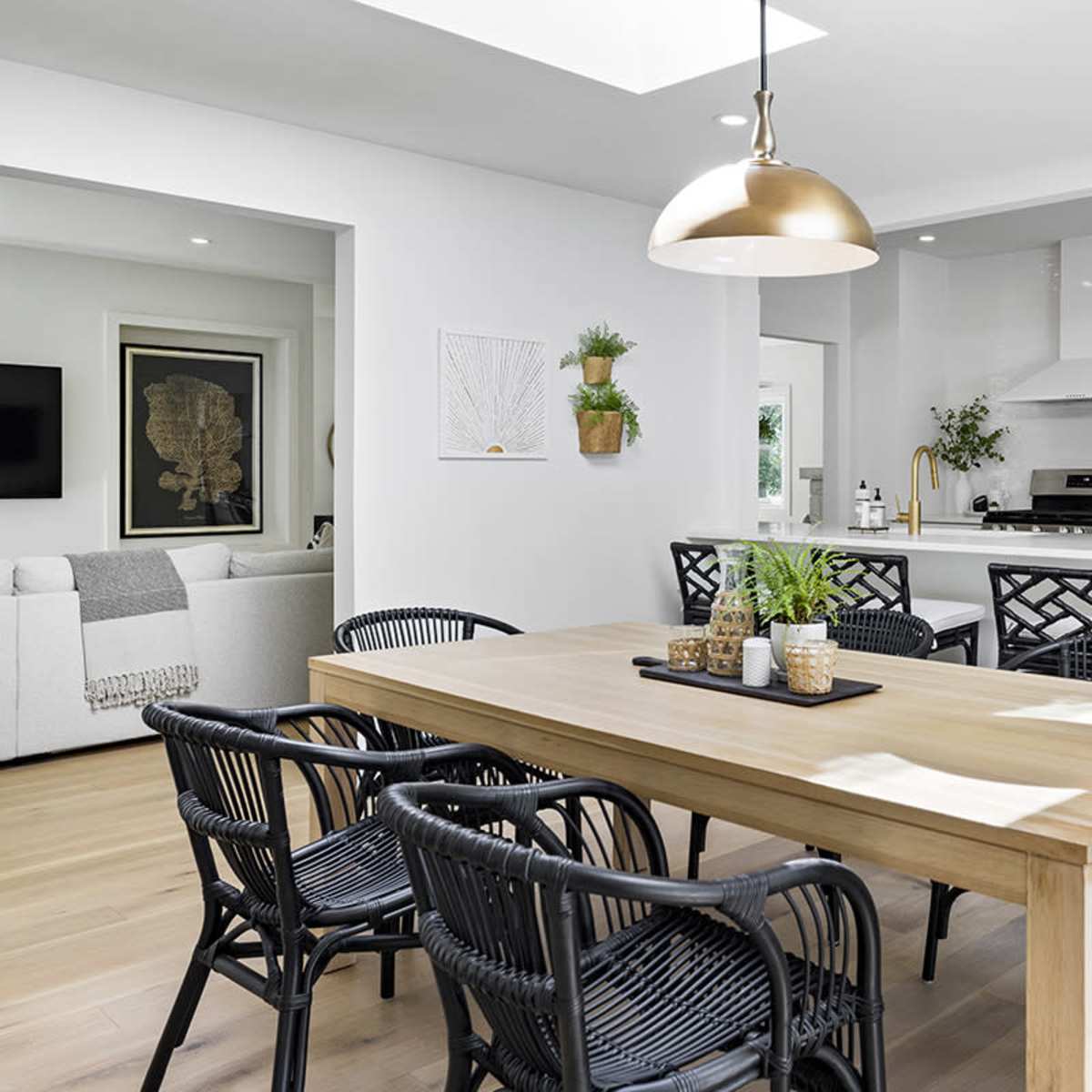 A spacious dining area features a wooden table surrounded by black woven chairs, adjacent to a modern kitchen with white cabinetry and stainless steel appliances.