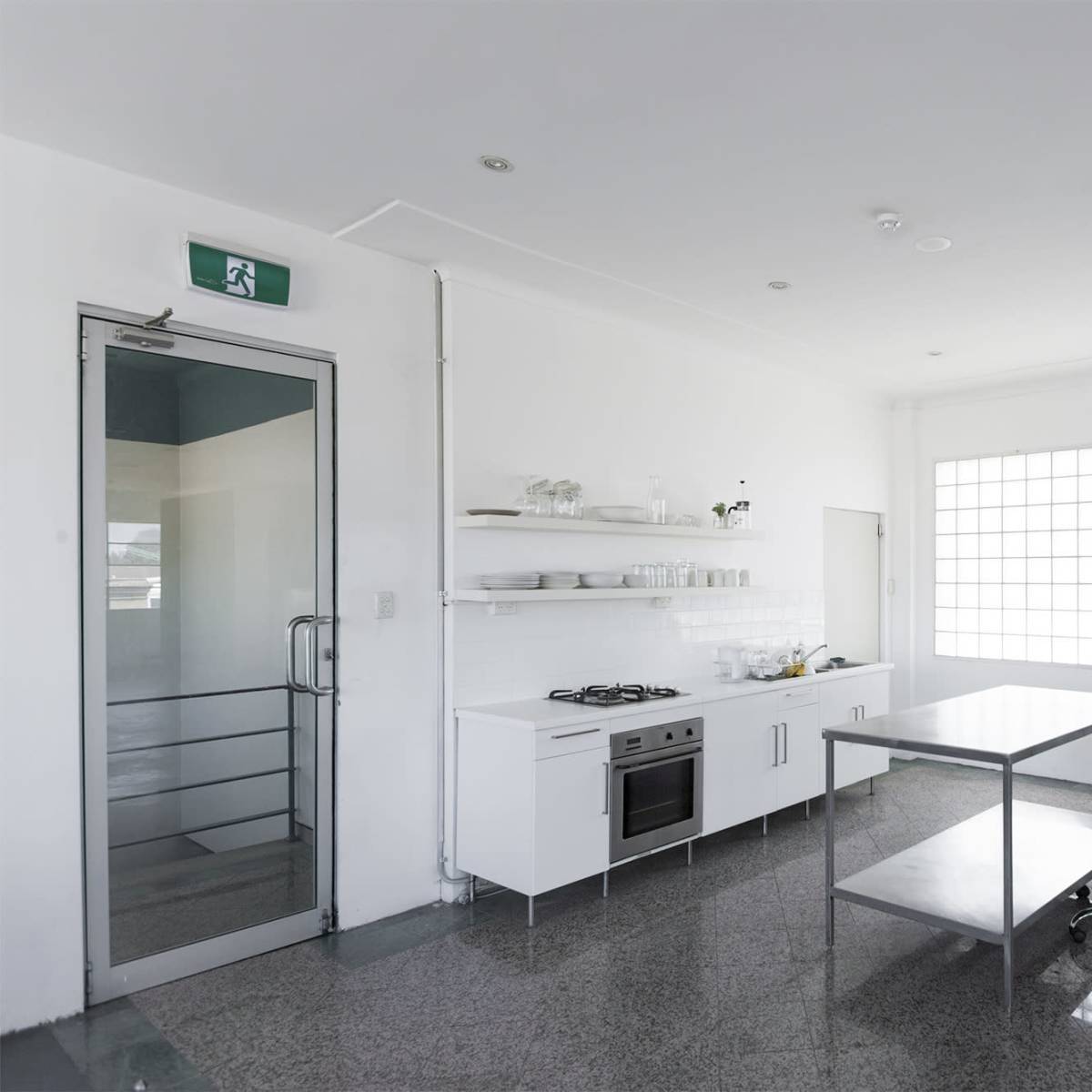 A modern kitchen features a glass door, a central table with a stool, and appliances against white cabinetry.