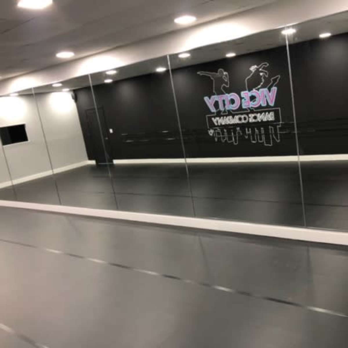 A spacious dance studio with mirrored walls and a black backdrop featuring the word "VIC CITY" in colorful lettering.