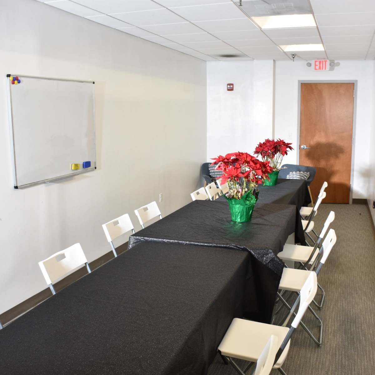 A long table covered in a black tablecloth is set up in a brightly lit meeting room with white walls and chairs on either side.