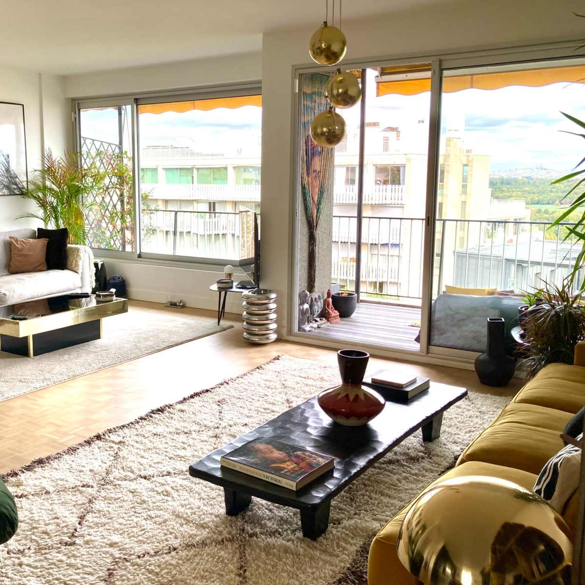 A modern living room features two sofas, a coffee table, and large windows overlooking a balcony with a scenic view.