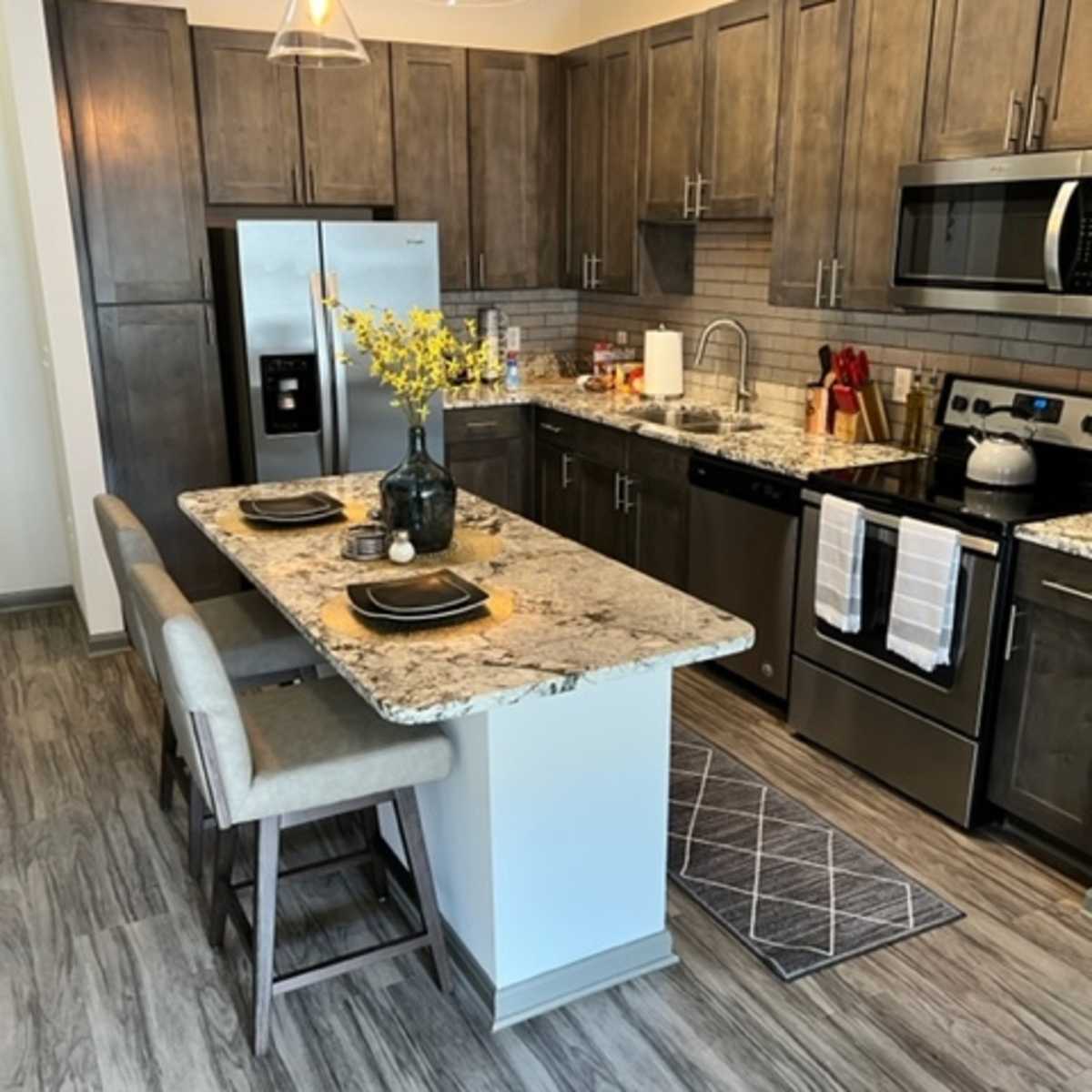 A modern kitchen with wooden cabinets, stainless steel appliances, a granite countertop, and a small island with seating.