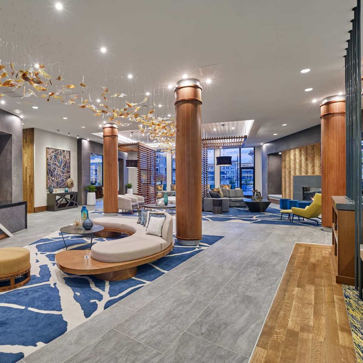 A modern lobby features large abstract art pieces, curved seating areas, wooden pillars, and a decorative ceiling installation.