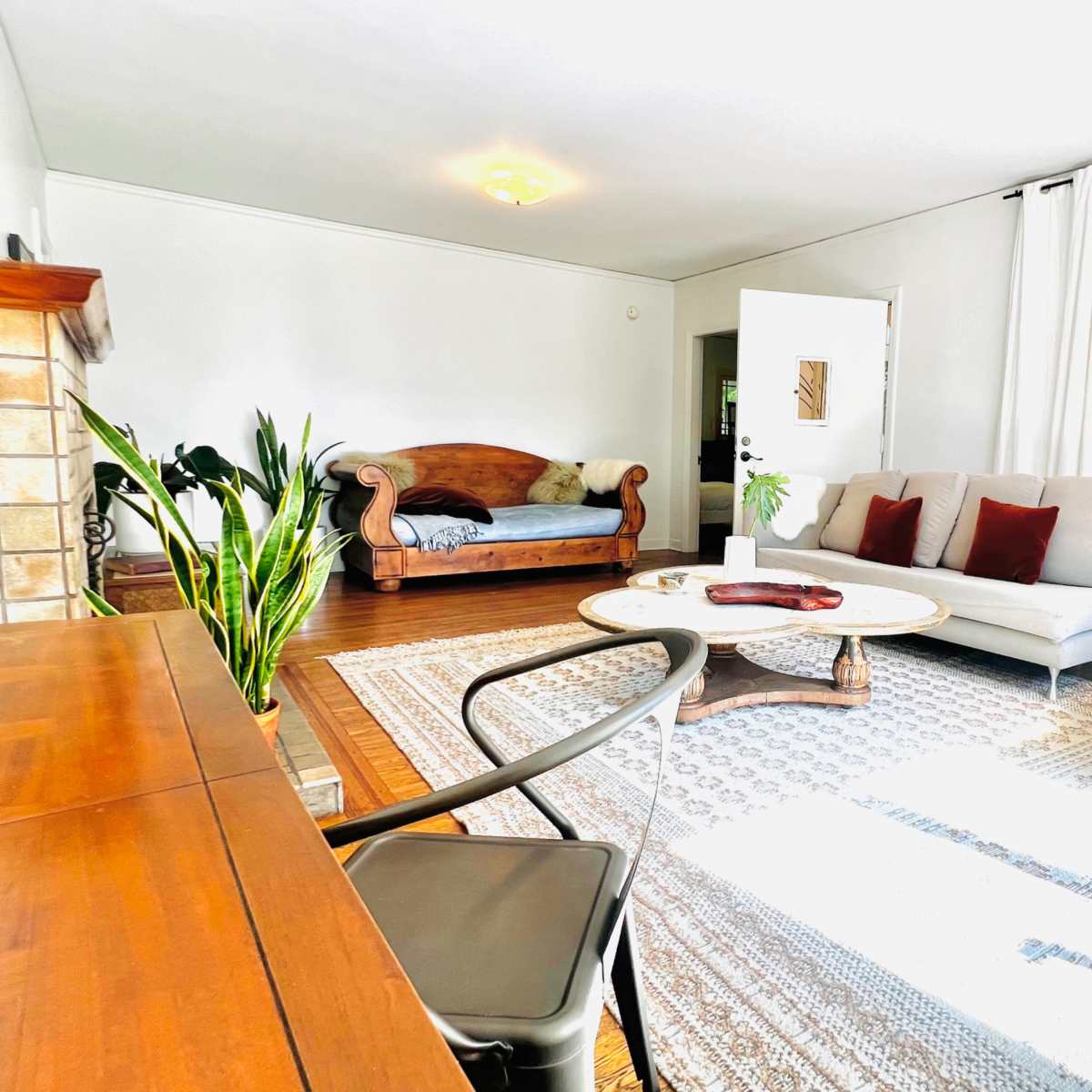 The room features a furnished living space with a wooden desk, two sofas, a circular coffee table, and large windows allowing natural light.