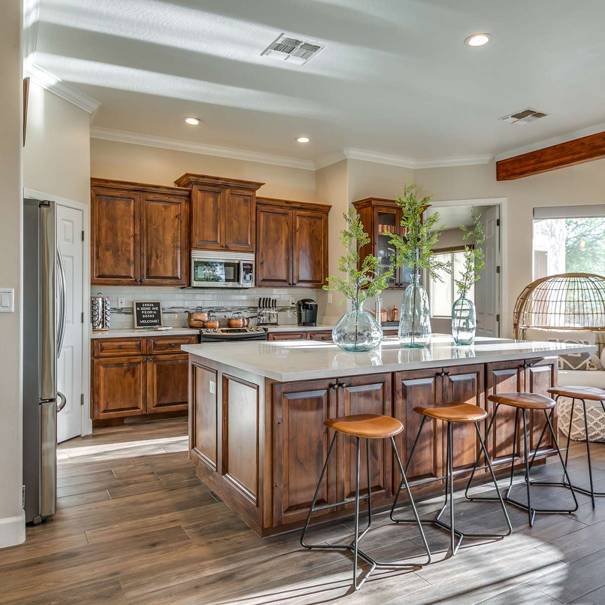 A modern kitchen with wooden cabinets, white countertops, and a central island with four bar stools.