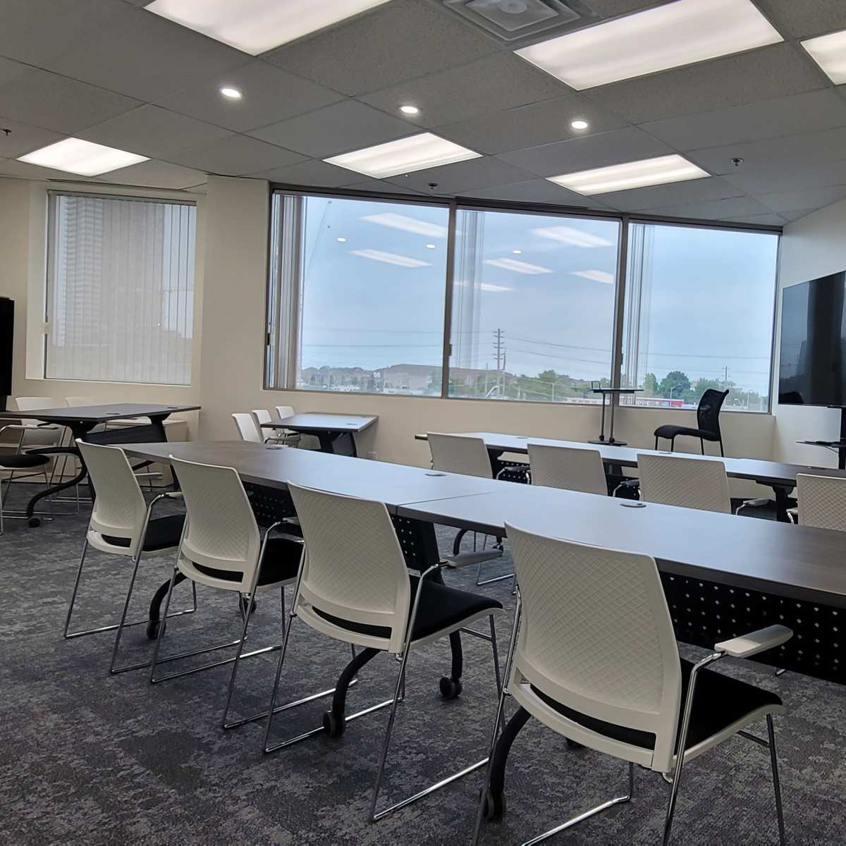 A modern conference room equipped with a long table, chairs, a large screen, and windows offering a view of the outdoors.