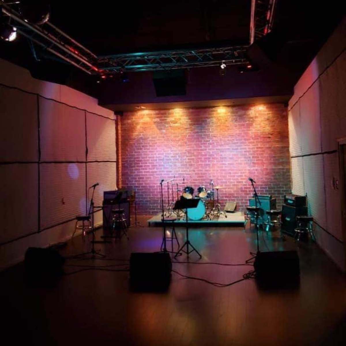 A dimly lit music stage with a brick wall backdrop, equipped with musical instruments and amplified speakers.