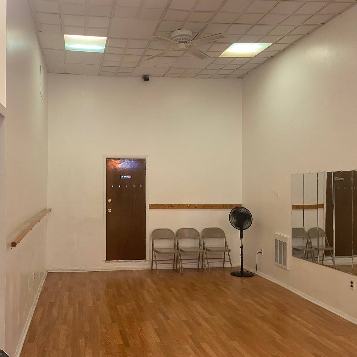 A spacious, empty dance studio with a wooden floor, a large mirror, and a door at the far end.