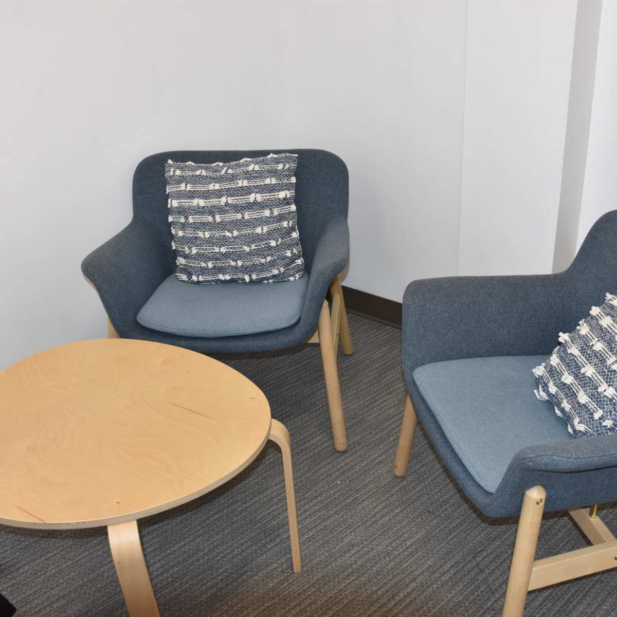 Two blue armchairs with patterned cushions flanking a small wooden table in a neutral-toned room.
