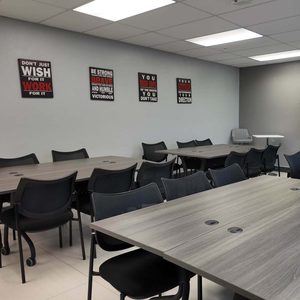 A modern conference room with multiple tables and chairs arranged neatly, along with motivational posters on the wall and a large screen at the front.