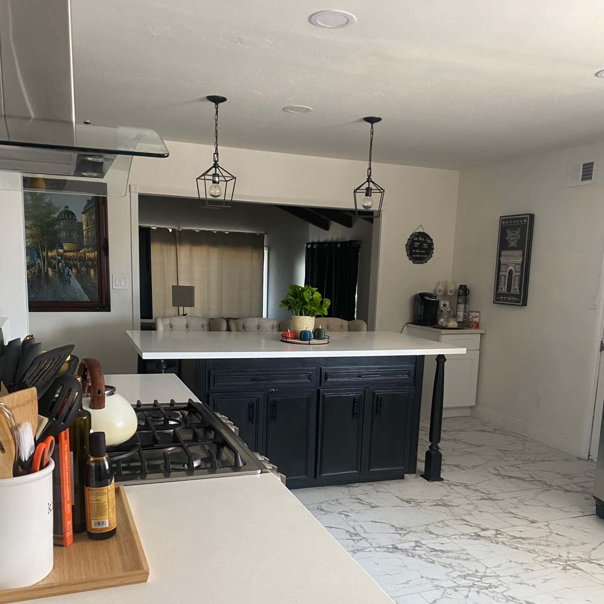 The kitchen features a central island with a black base and white countertop, surrounded by cabinets and marble flooring.