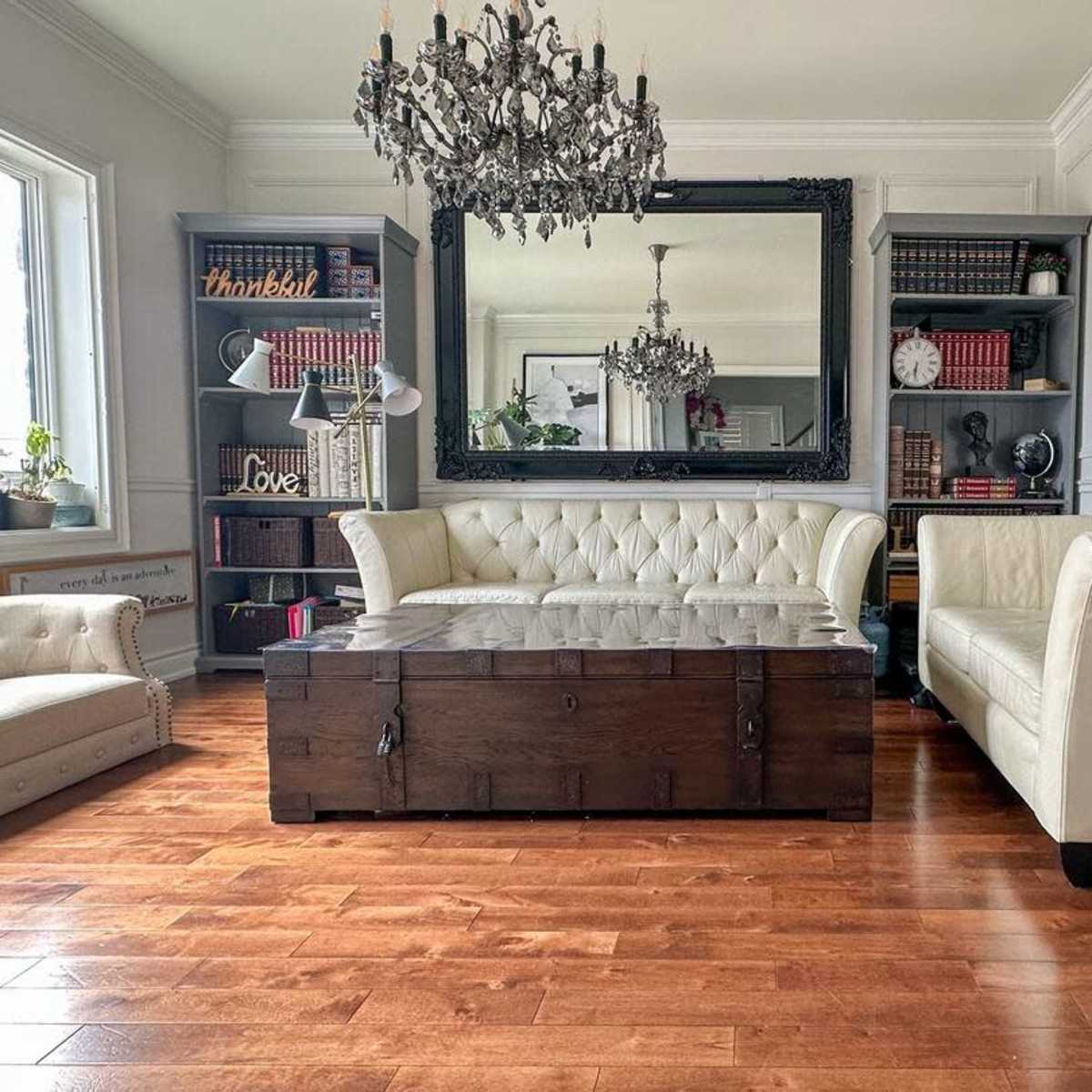 A well-furnished living room with a chandelier, a large mirror, two sofas, a wooden coffee table, and a bookshelf against the wall.