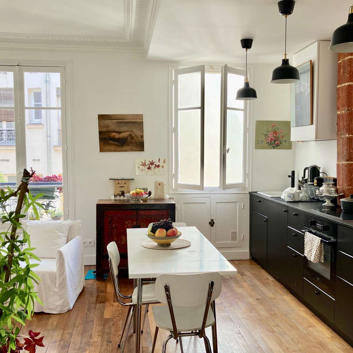 A modern kitchen features black cabinetry, a white dining table with chairs, and large windows illuminating the space.