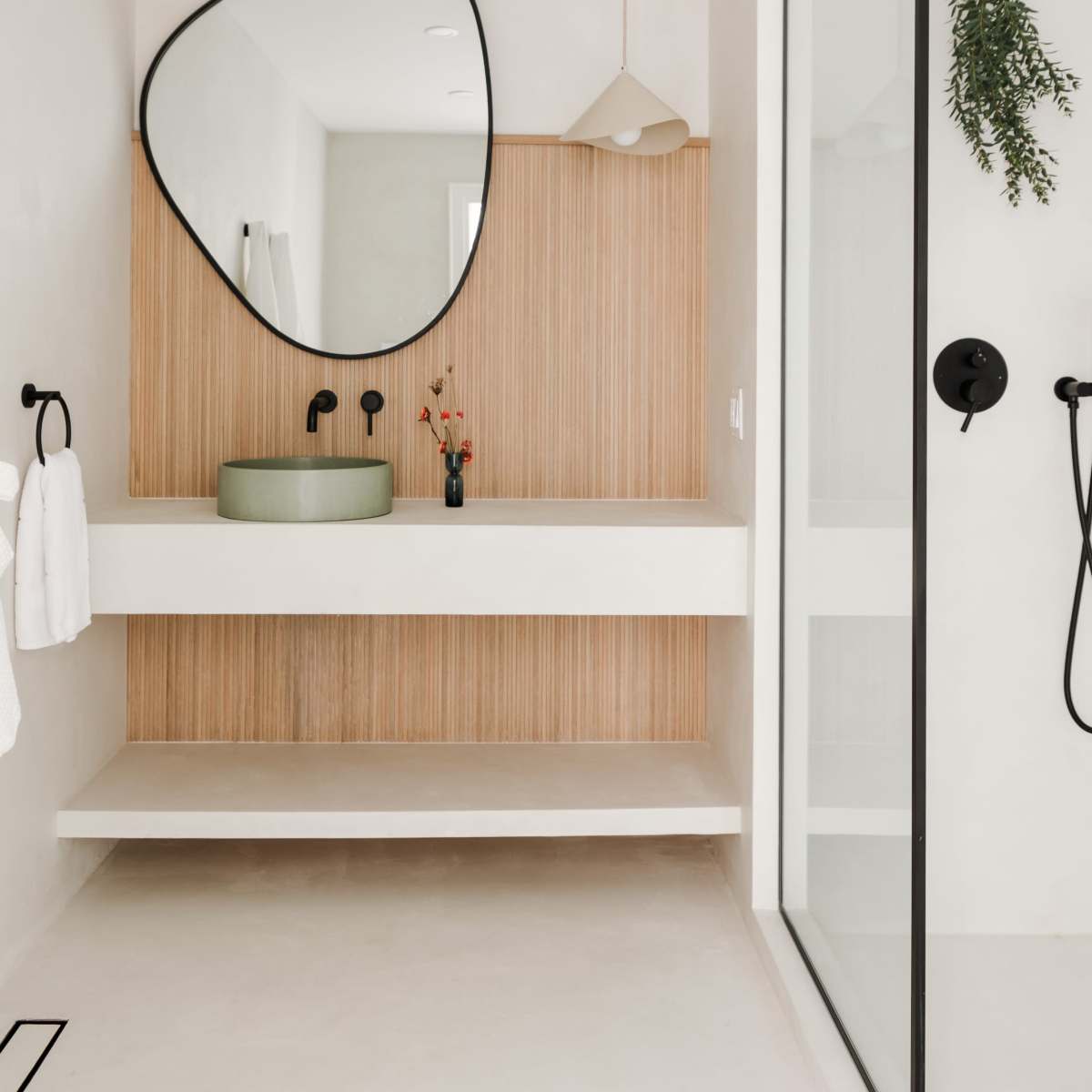 A modern bathroom featuring a green basin on a floating countertop, a large mirror, and a glass shower enclosure.