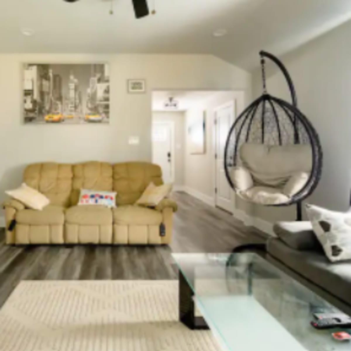The living room features a beige recliner sofa, a hanging chair, a glass coffee table, and modern decor on the walls.