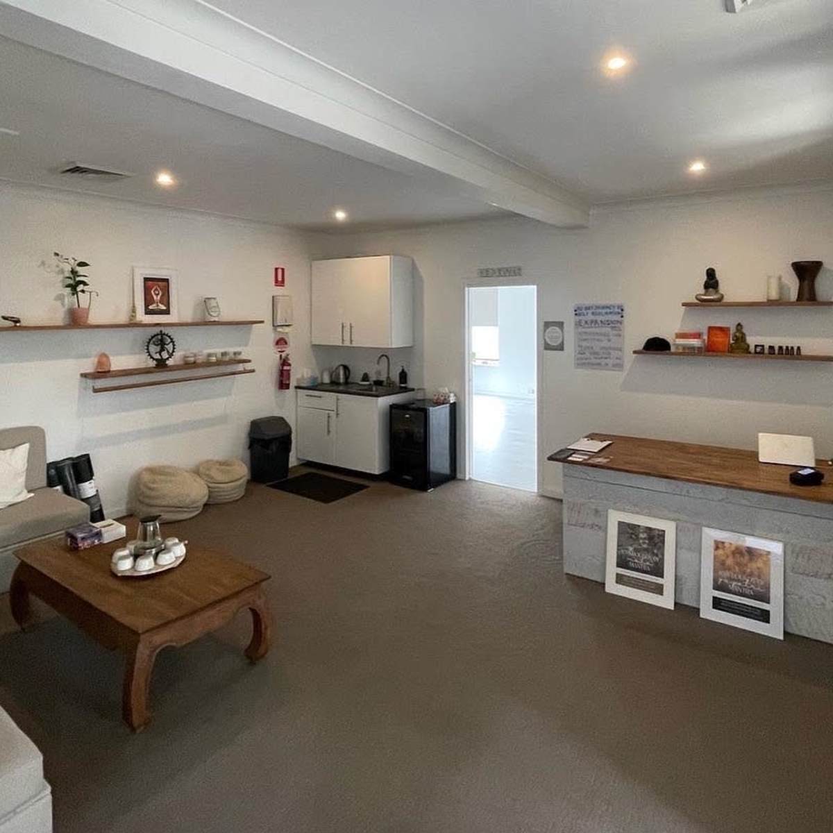 A modern, minimalist interior of a room featuring a sofa, a coffee table, a kitchenette, and shelves with decorative items.