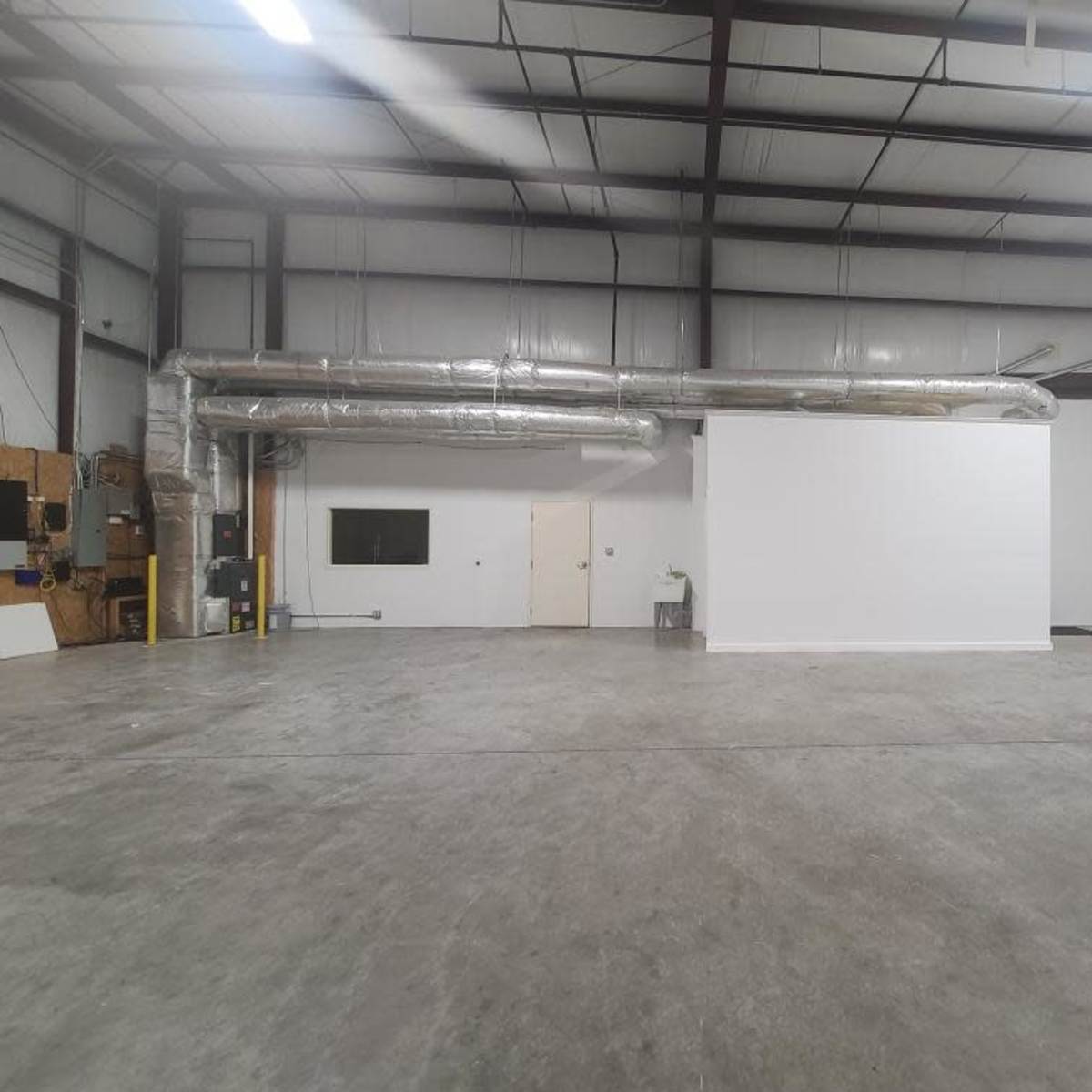 An empty industrial warehouse space with high ceilings, exposed ductwork, and a concrete floor.