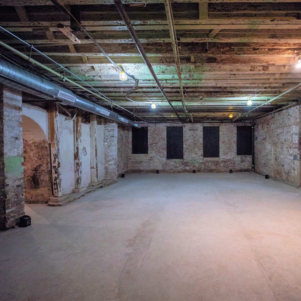 A large, empty basement room with exposed stone walls, a concrete floor, and overhead lighting.