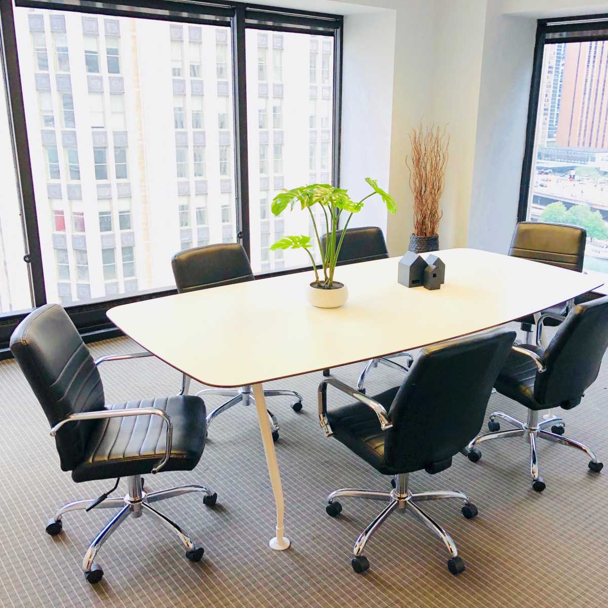 A modern conference room features a white oval table surrounded by black office chairs, with large windows offering a view of the city.