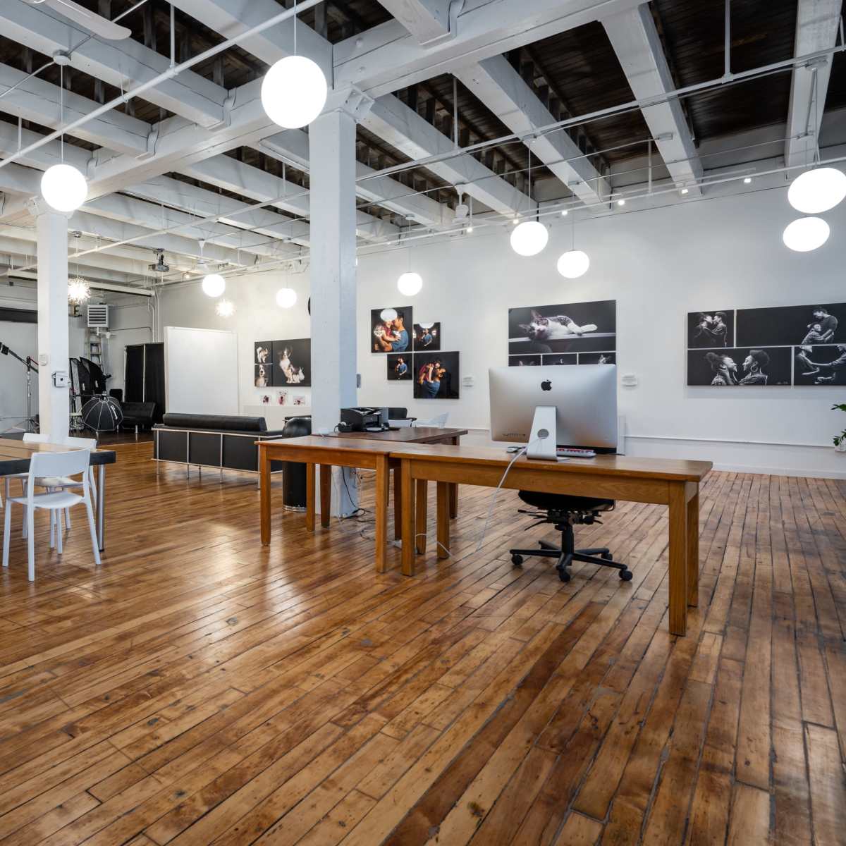 A spacious office area with wooden flooring, a large table with white chairs, and photographic displays on the walls.