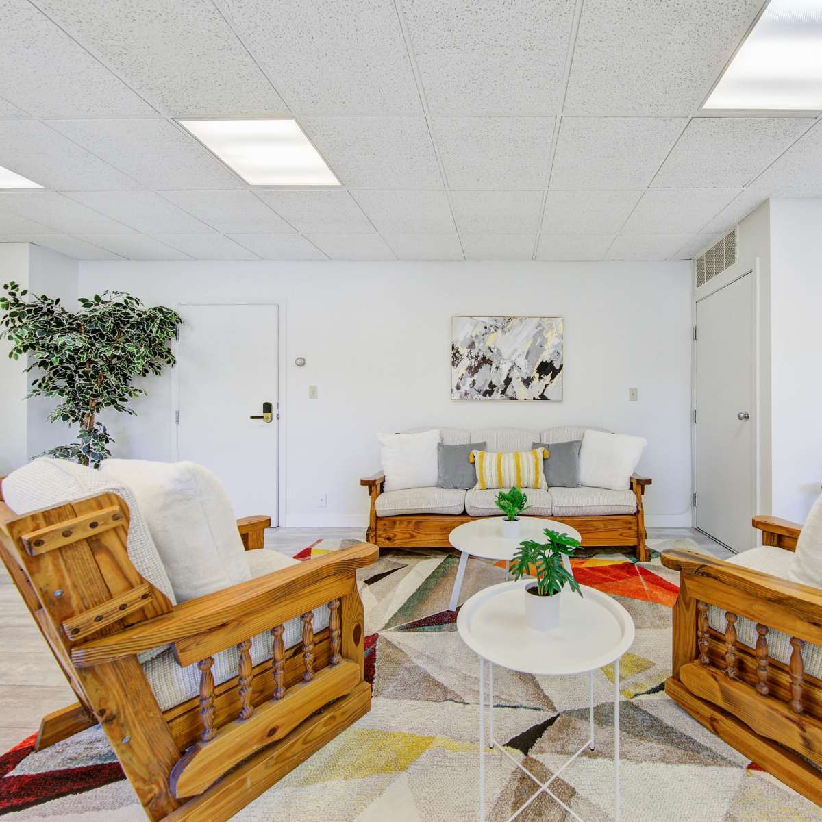 A modern living room features two wooden rocking chairs, a small table, a colorful area rug, and a plant in a corner.