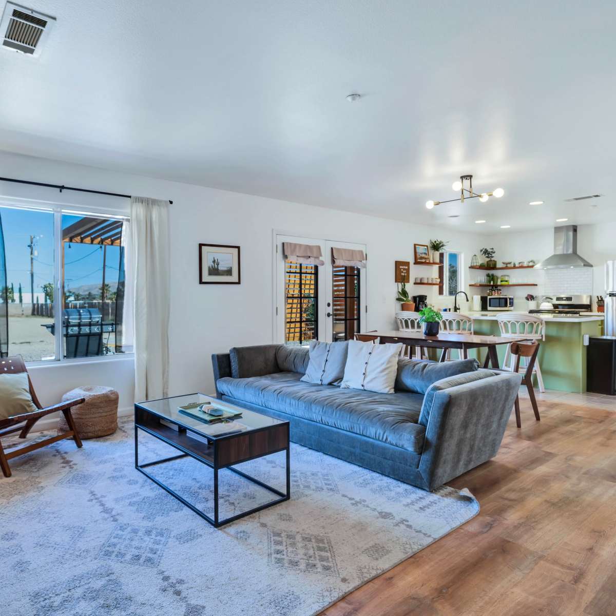 A modern, open living space with a gray sofa, a coffee table, and a view of a landscaped outdoor area through a large window.