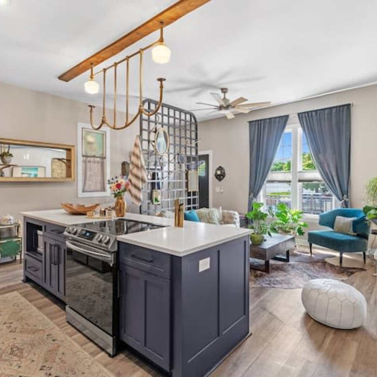A modern kitchen features a central island with a stove, adjacent to a living area with a green sofa and large windows.