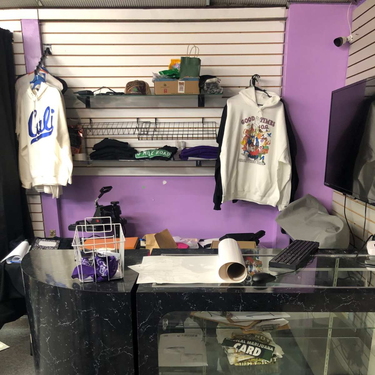 A retail display area with a curved counter, shelves containing clothing items, and a television mounted on the wall.
