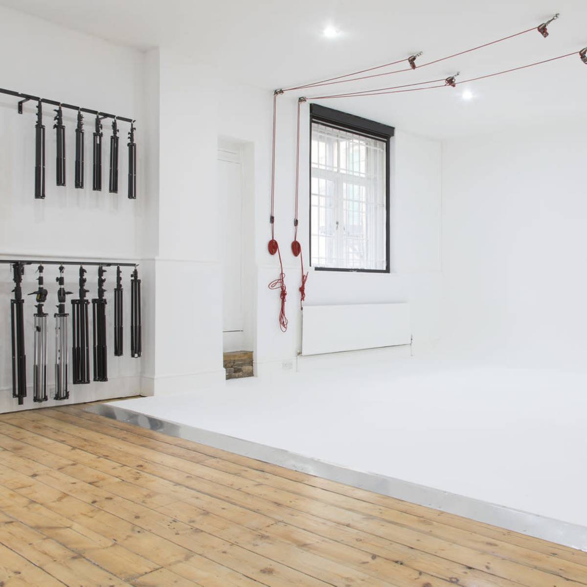 A white studio space with a wooden floor, equipped with various hanging props along one wall and a raised white platform in the center.