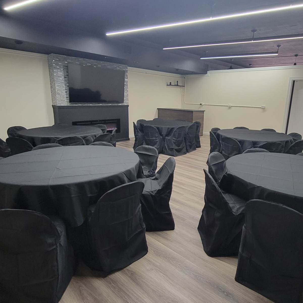 A room set up for an event, featuring several round tables covered with black tablecloths and matching chairs arranged around them.