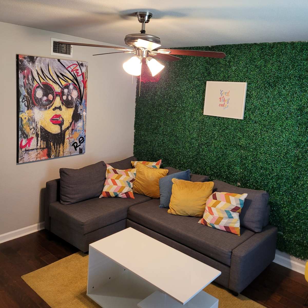 A living room with a gray sectional sofa adorned with colorful pillows, a white coffee table, and a green moss wall accent.