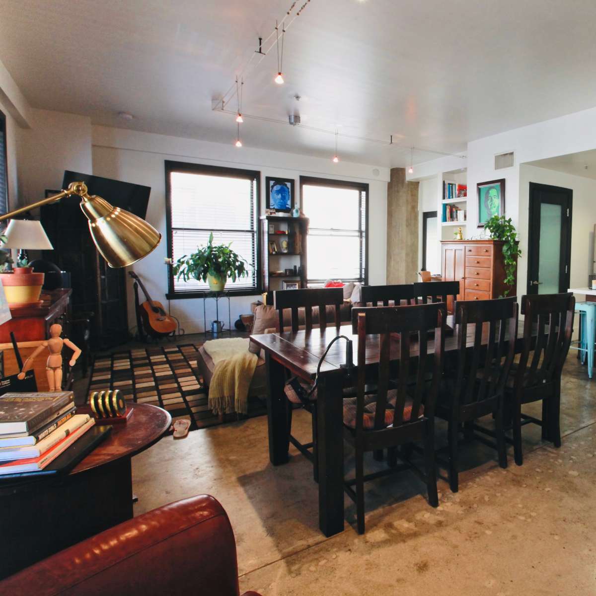 An open-concept living and dining area with a wooden dining table, kitchen with modern appliances, and a seating area featuring a guitar and plants.