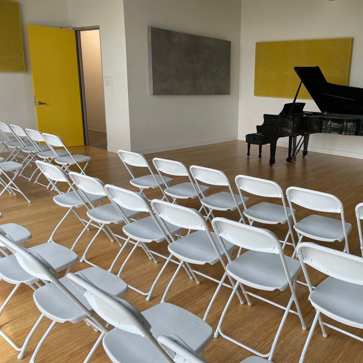 A room with a grand piano, a small piano, and several rows of white folding chairs set up in front of them.
