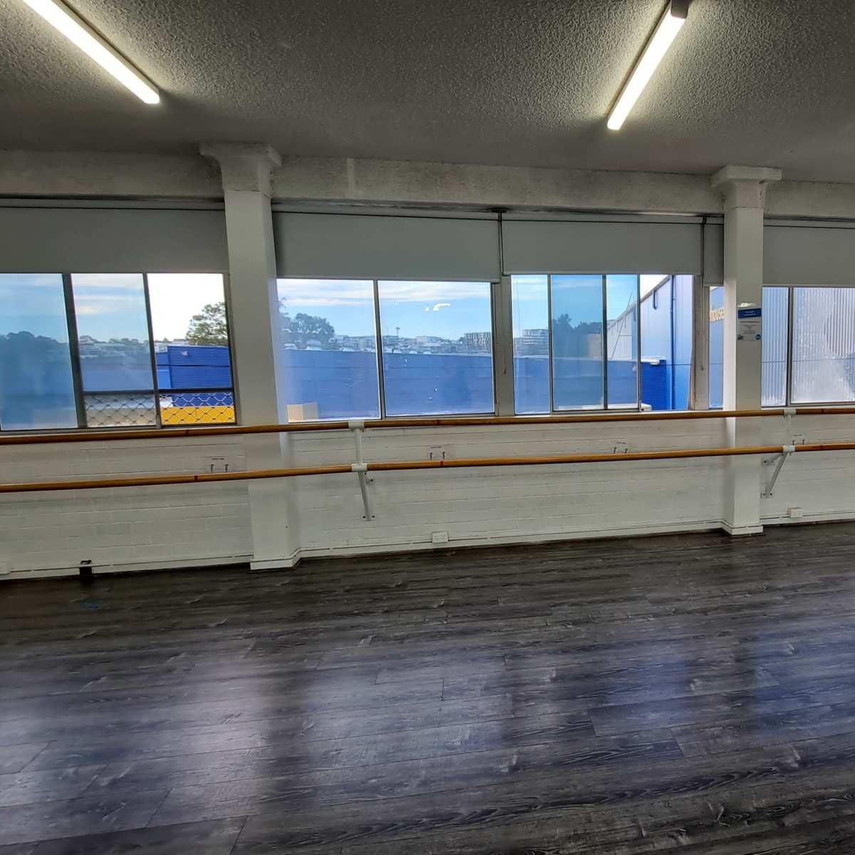 A spacious dance studio with large windows, wooden flooring, and a ballet barre along one wall.