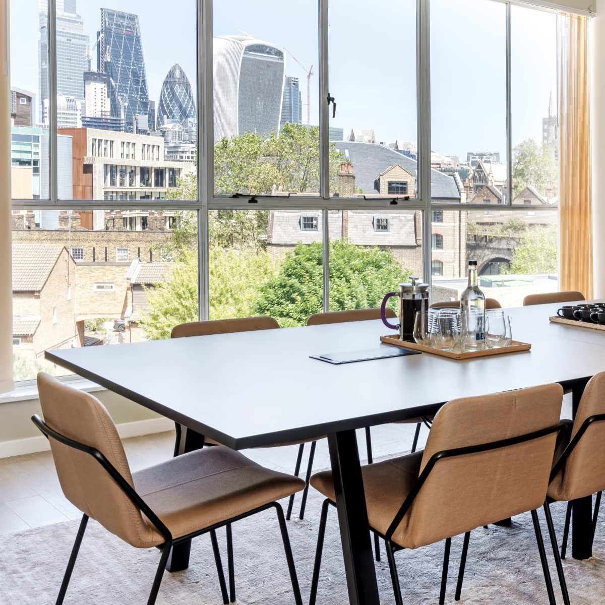 A modern dining area features a large table set with a tray of drinks, overlooking a city skyline through large windows.