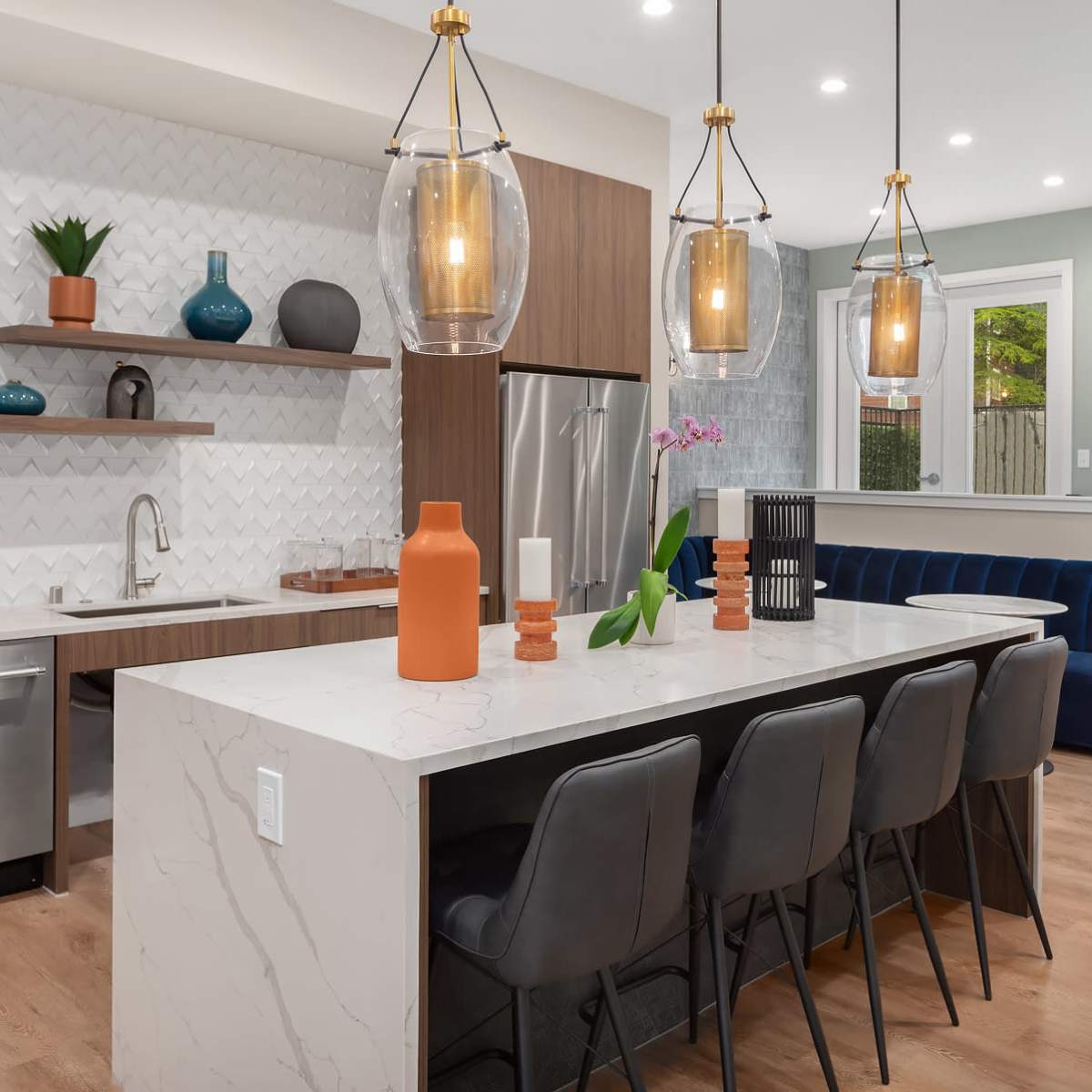 A modern kitchen with a large island, featuring pendant lights, bar stools, and a mix of wooden and white cabinetry against a textured backsplash.