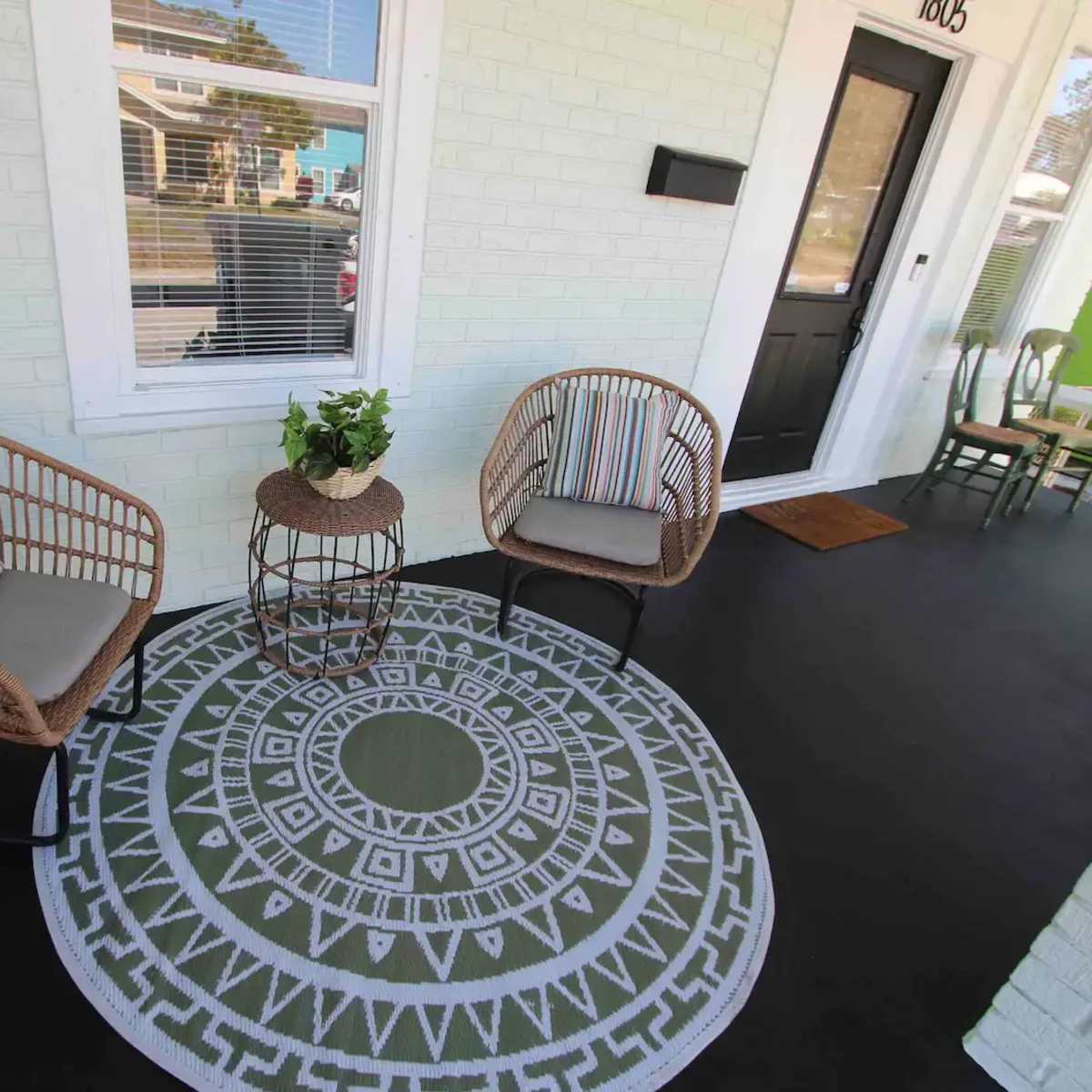 A porch area featuring two wicker chairs with cushions, a round decorative table, and a patterned outdoor rug.