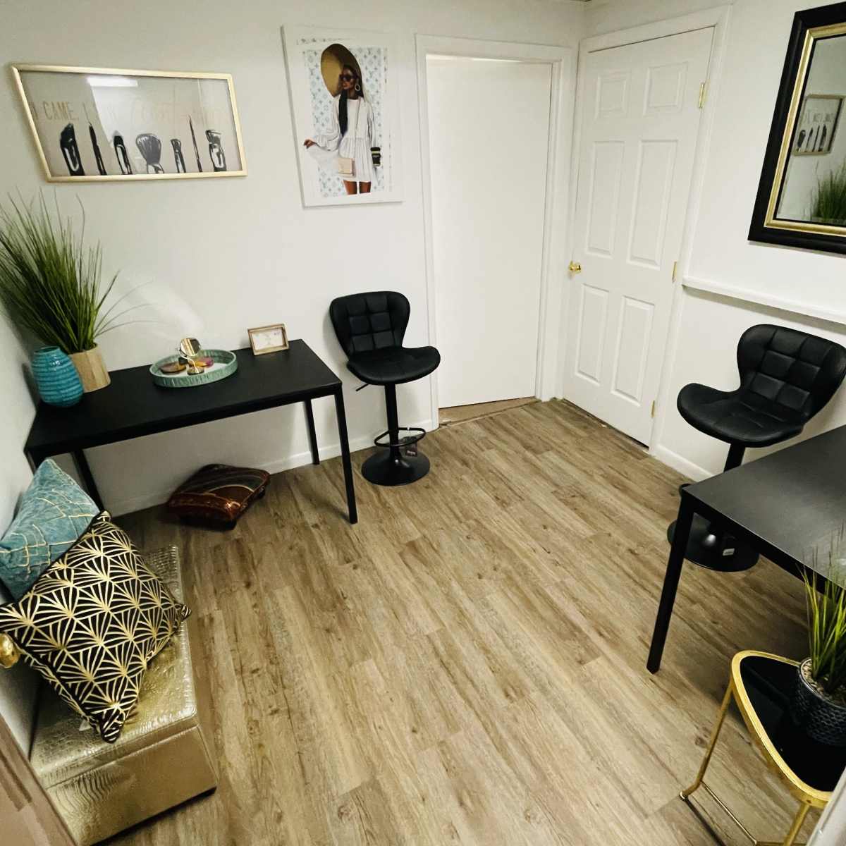 A small room with two black tables, two black stools, decorative plants, and a wall adorned with art.