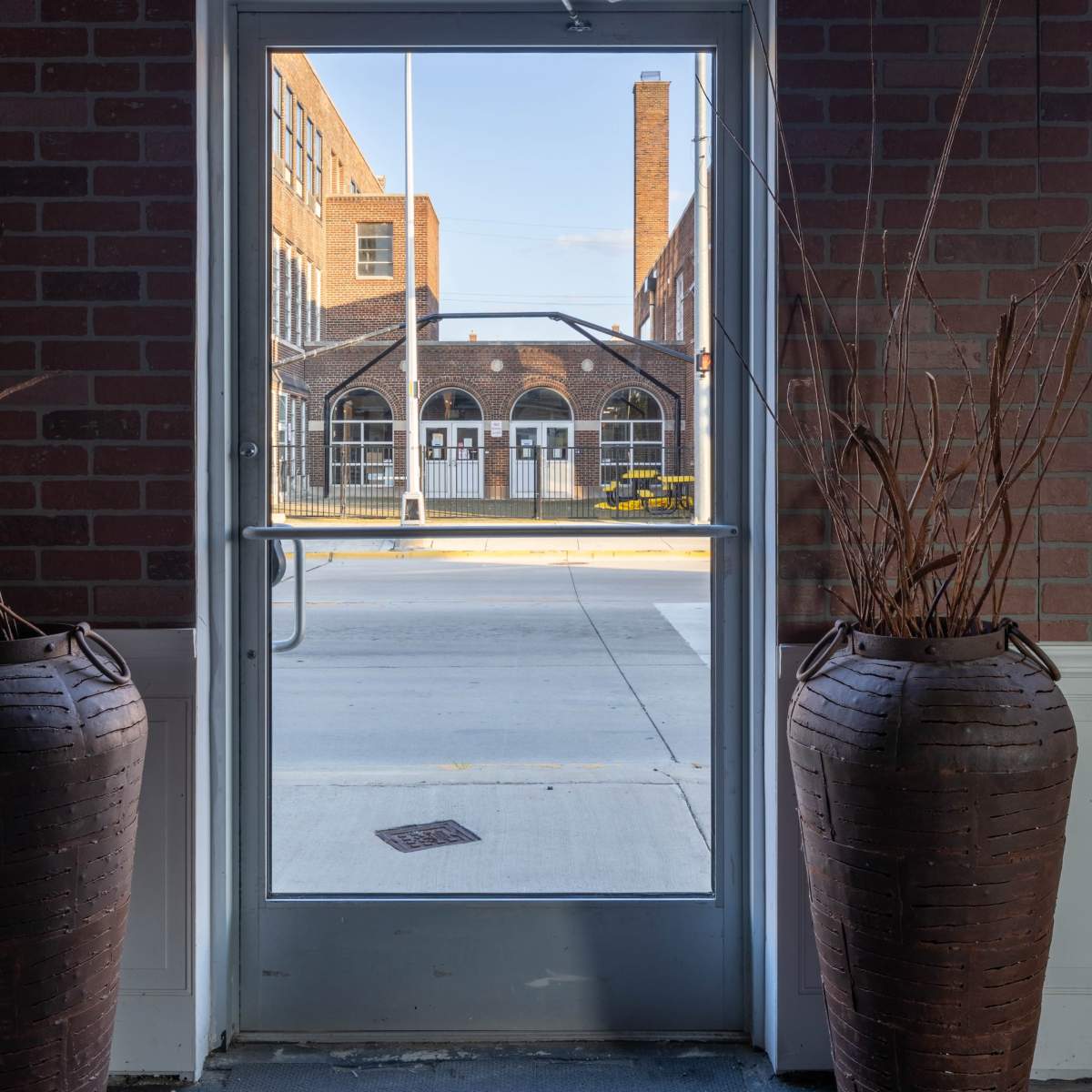 A view through a doorway framed by two large pots, revealing a brick building across a street.