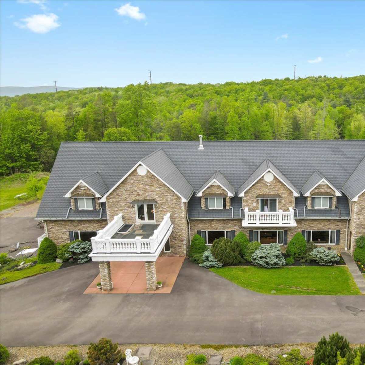 A large, stone-faced building with multiple sections and balconies, surrounded by landscaped greenery and a paved driveway.
