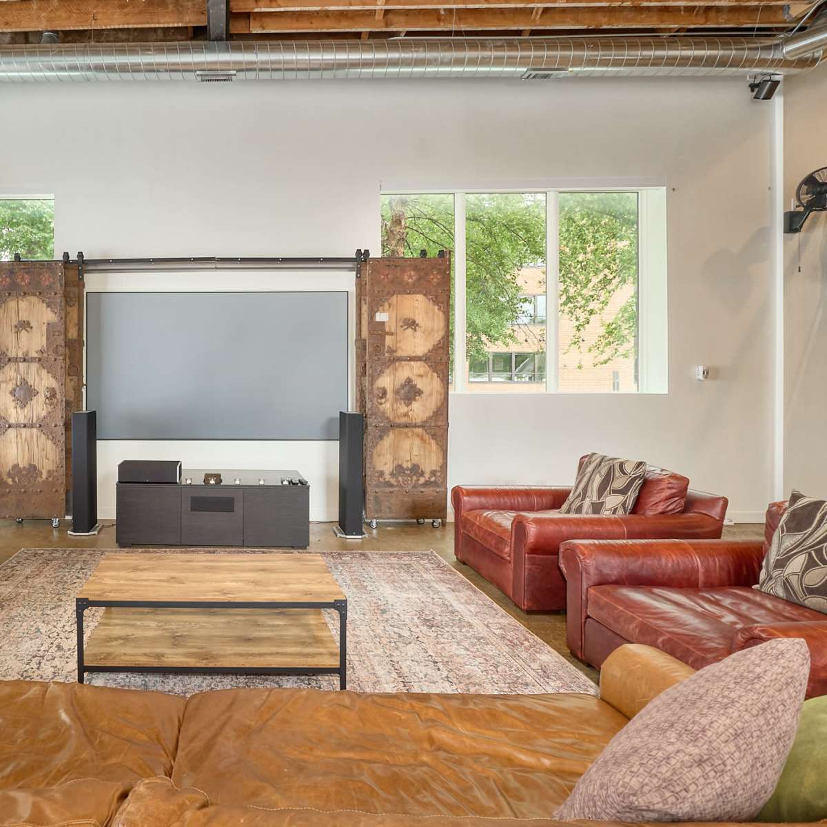 A spacious living room with two red leather sofas, a wooden coffee table, and a large screen mounted on the wall, flanked by decorative dividers.