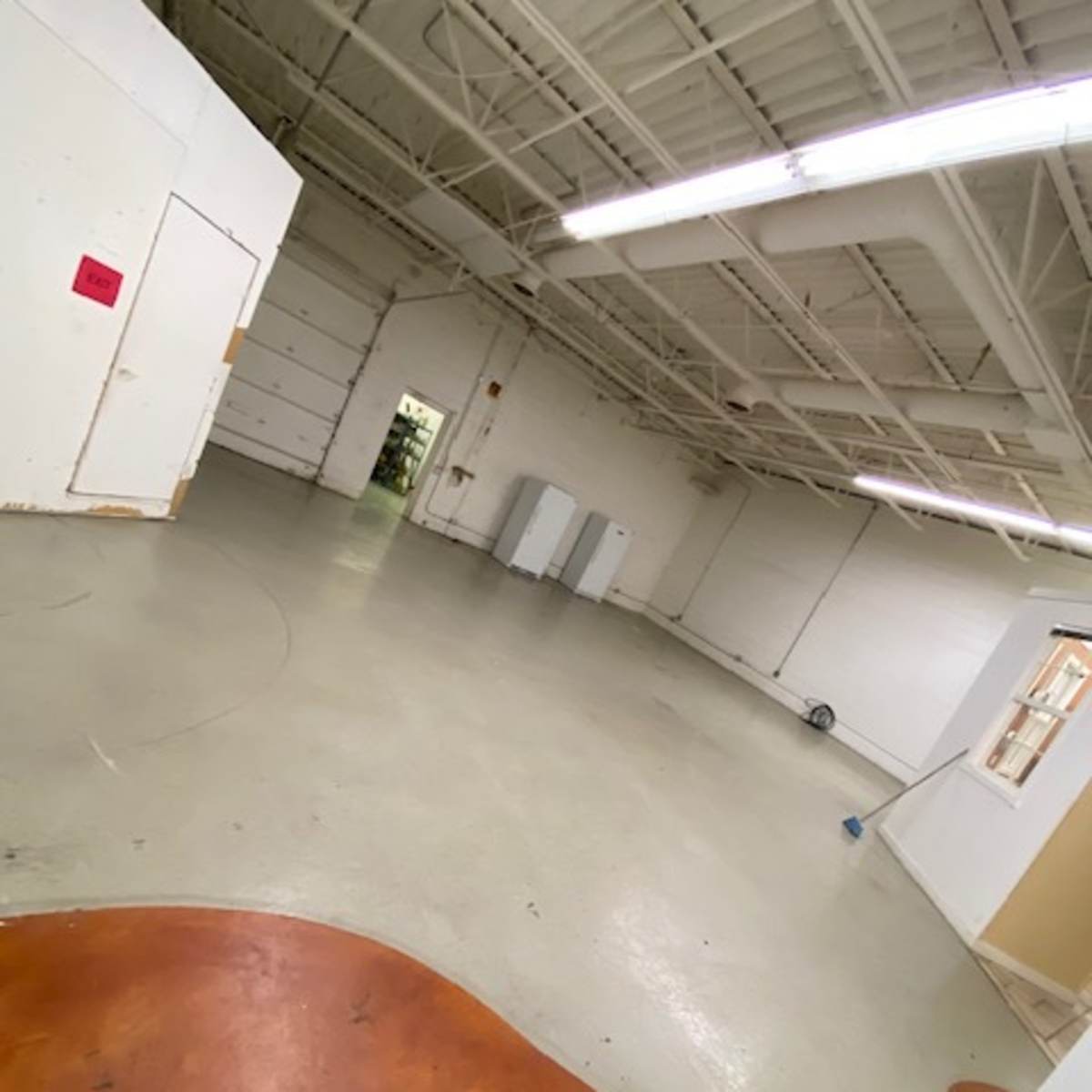 A spacious, empty room with a polished concrete floor and white walls, featuring a distinct orange floor area in the foreground.