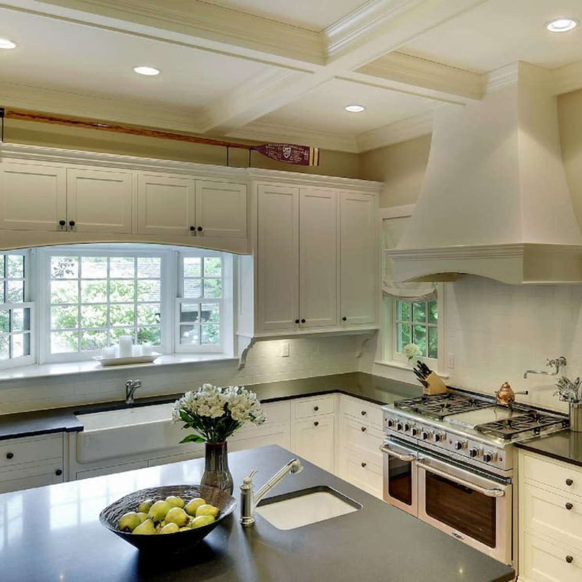 A modern kitchen features white cabinetry, a center island with a bowl of lemons, and a large window overlooking greenery.